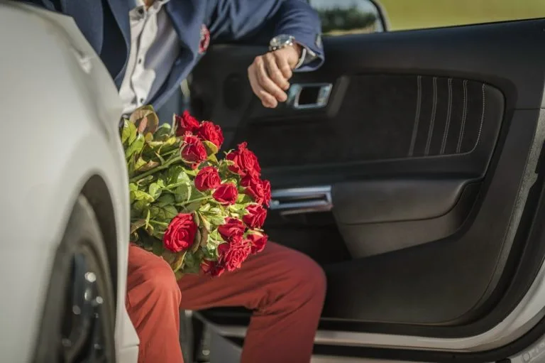 Blumen transportieren – Mann sitzt im Auto mit einem großen Strauß roter Rosen auf dem Schoß