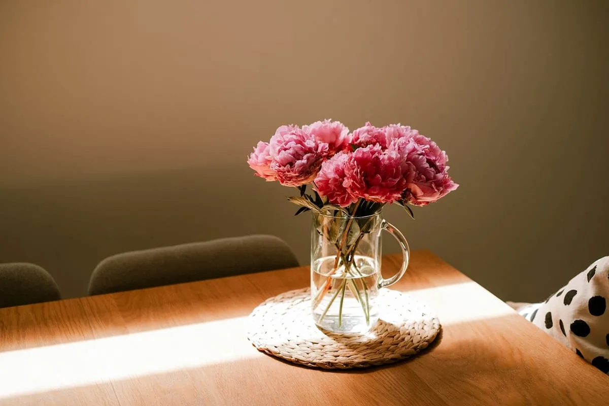 Strauß rosa Pfingstrosen in einer Glasvase auf einem sonnigen Tisch